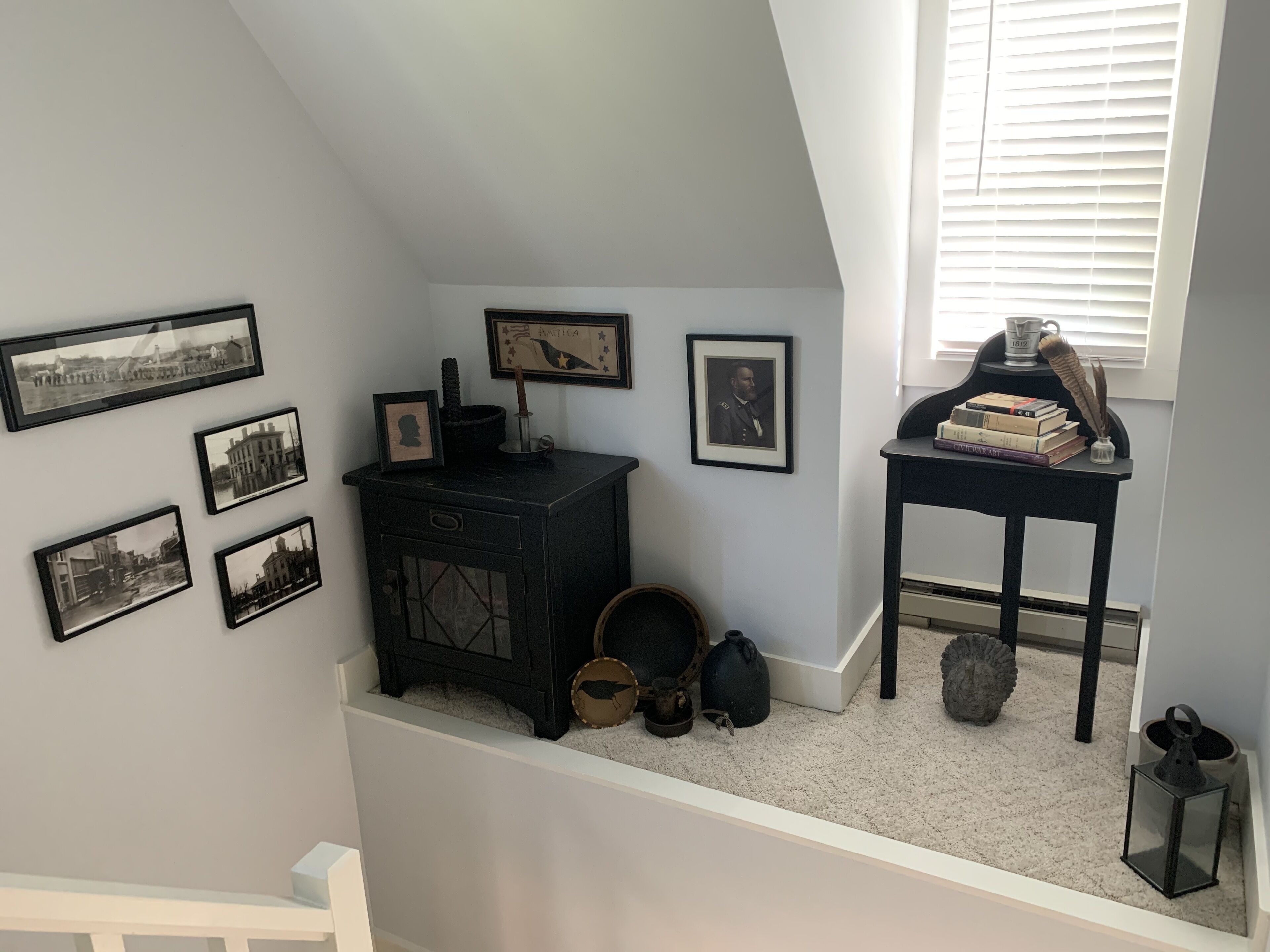 A room with a black dresser, a small table with books and a teapot, and several framed photographs on the wall.