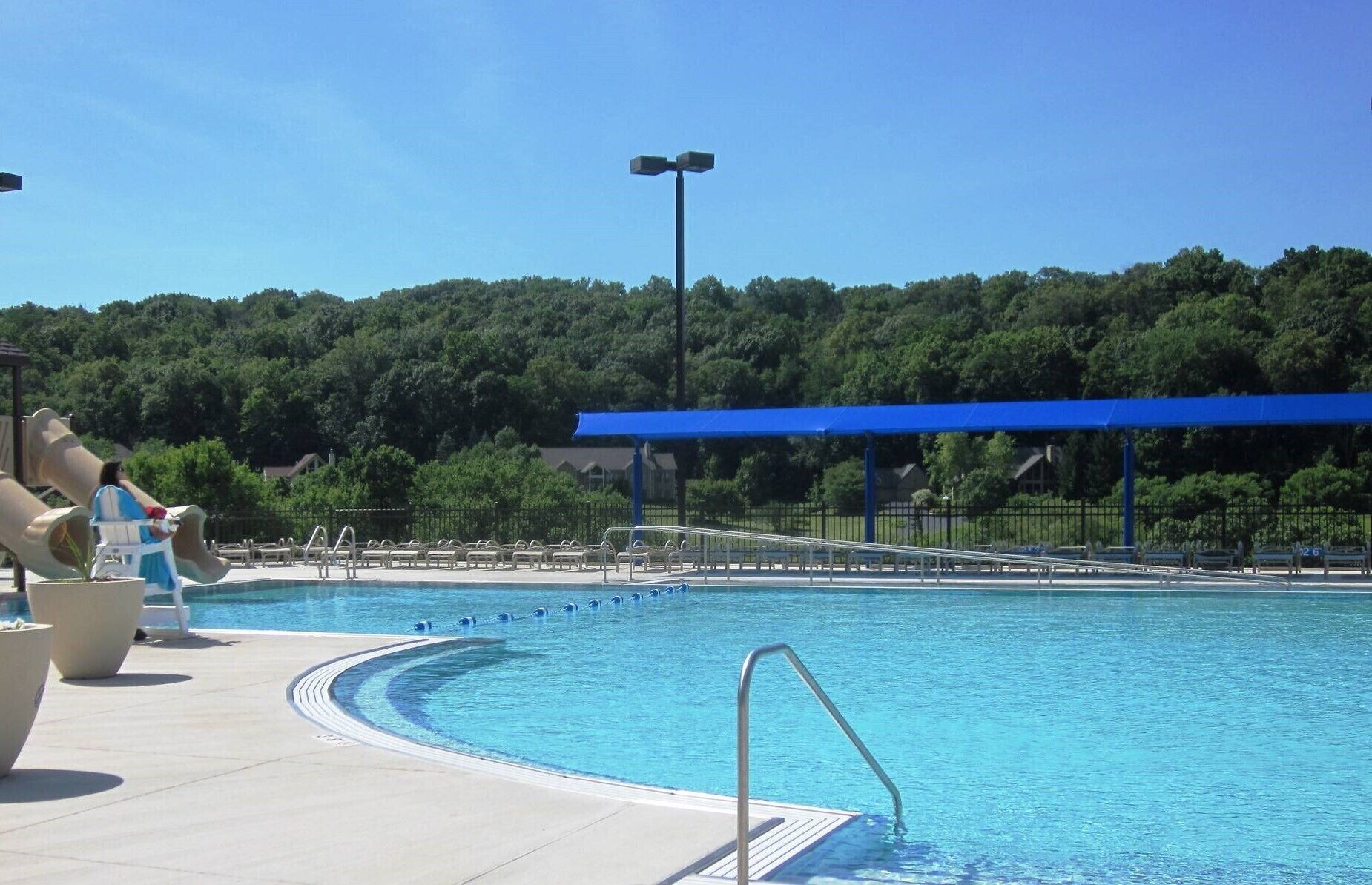 Une piscine surmontée d’un auvent bleu, avec des chaises longues et une rambarde en métal.