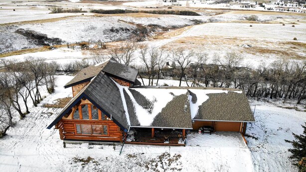 Une cabane en rondins avec un toit pentu et une grande véranda, entourée d’un paysage enneigé.