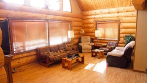 L’intérieur d’une cabane en rondins, avec un plancher en bois, deux canapés, un fauteuil, une table basse et une lampe.