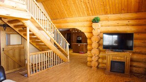 L'intérieur d'un chalet en bois, avec un escalier en bois, un téléviseur et une cheminée.