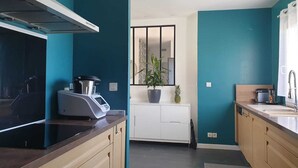 A modern kitchen with teal walls, a black stove, a white cabinet, and a potted plant.