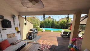An outdoor patio area with a wooden deck, a barbecue grill, a pool, and lounge chairs.