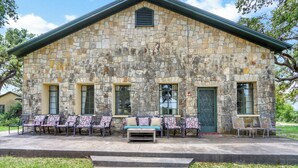 A stone building with a porch, outdoor seating, and a staircase leading up to the entrance. - Live Oak Ranch - Swimming Pool Property with Sleeping for 20! (Spring Branch)