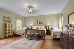 A bedroom with two beds, a wooden dresser, a chest of drawers, a ceiling fan, and a large mirror.