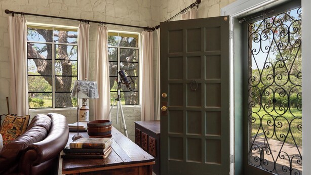 A cozy room with a leather sofa, a wooden table with books and a lamp, and a door with a wrought iron gate. - Live Oak Ranch - Swimming Pool Property with Sleeping for 20! (Spring Branch)