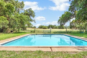 A rectangular swimming pool with a tiled edge, surrounded by grass and trees.