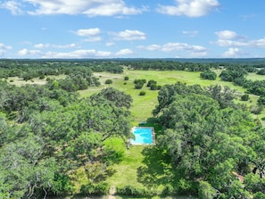 Vue aérienne d’une propriété dotée d’une piscine, entourée d’une végétation luxuriante et d’arbres.