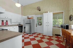 Una cocina con armarios blancos, un refrigerador, un microondas y piso de cuadros.