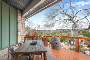 Una terraza de madera con una mesa y sillas, con vista a un paisaje con árboles y una estructura de piedra.