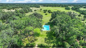 An aerial view of a property with a swimming pool surrounded by lush greenery and trees. - Live Oak Ranch - Swimming Pool Property with Sleeping for 20! (Spring Branch)