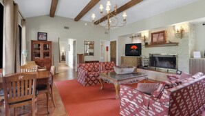 A spacious living room with a fireplace, a chandelier, and patterned furniture. - Live Oak Ranch - Swimming Pool Property with Sleeping for 20! (Spring Branch)