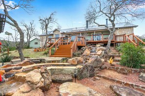 Una casa moderna con fachada de piedra, terraza de madera y una escalera de piedra que lleva a otra terraza de madera.
