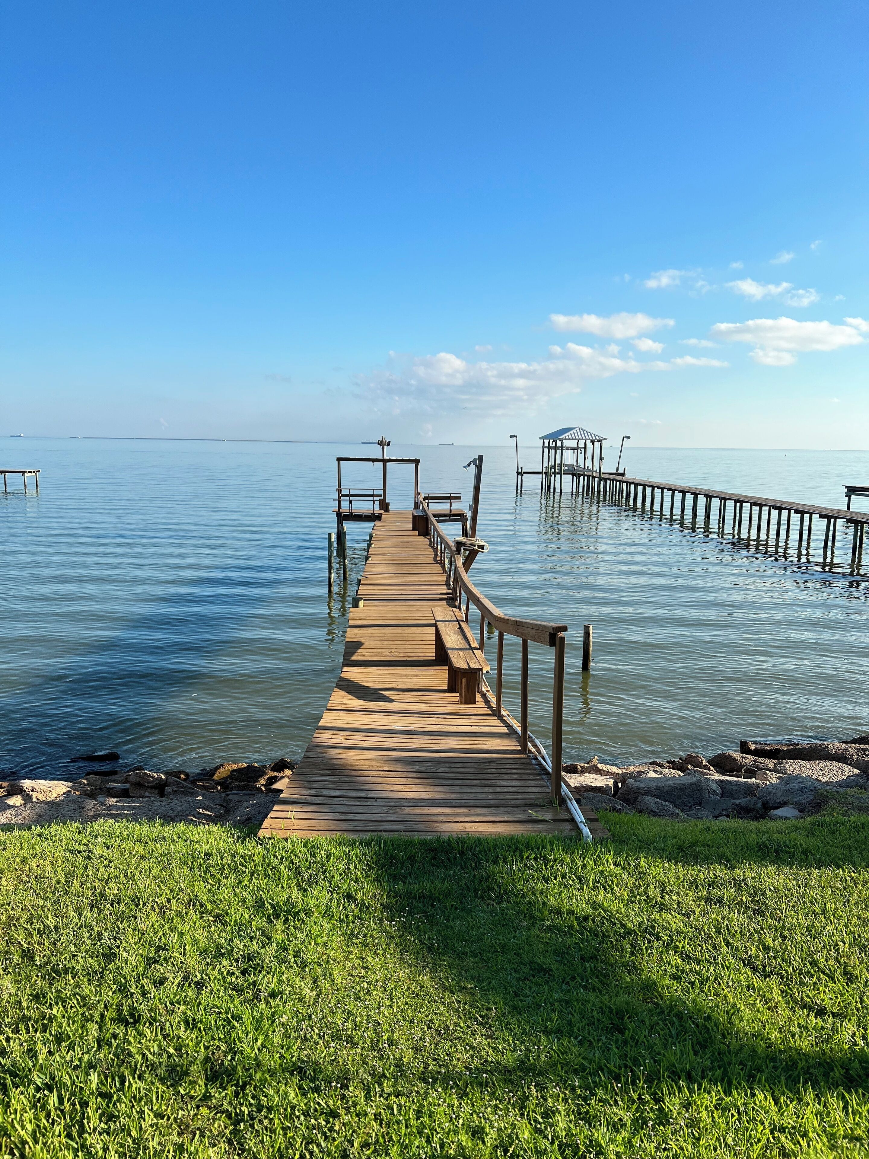 A wooden pier extending into calm water, with a grassy area in the foreground.