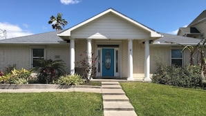 Une maison d’habitation avec une porte d’entrée bleue, des colonnes blanches et une pelouse bien entretenue.