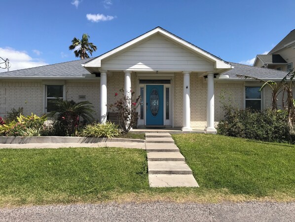 Una casa residencial con puerta azul, columnas blancas y césped bien cuidado.