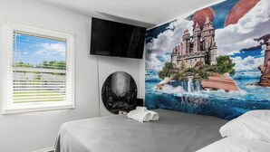 A hotel room with a bed, a TV mounted on the wall, a window with blinds, and a large mural of a castle on the wall. - ★Dragon’s Lair★Private Home w/ Arcade & Minigolf★ (Westerville)