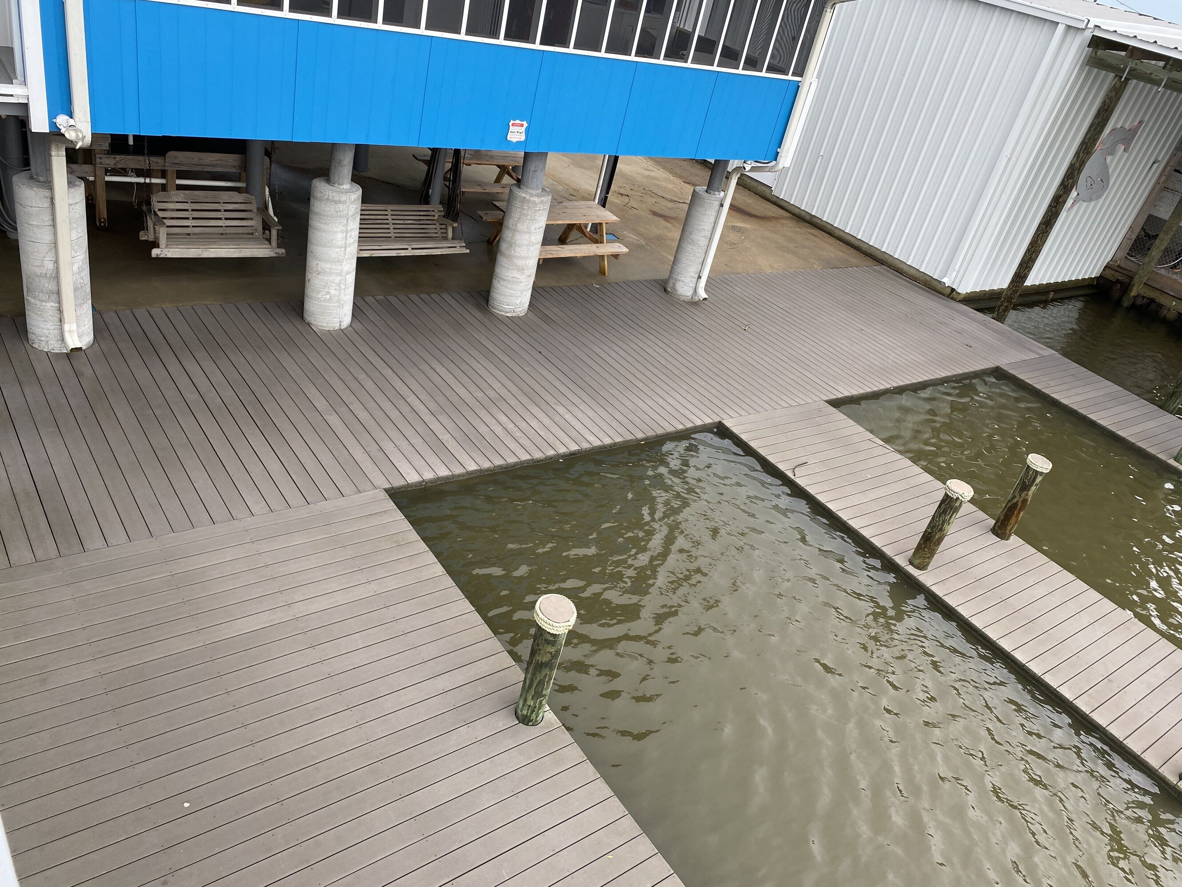 A wooden dock with a blue structure overhead, concrete pillars, and a small water feature.