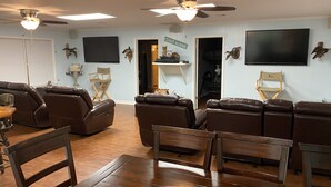 A living room with leather recliners, a wooden coffee table, a flat-screen TV, ceiling fans, and a 'Coast Along' sign. - Prime spot located on the water, Luxury living Bayou front living at its finest. (Chauvin)