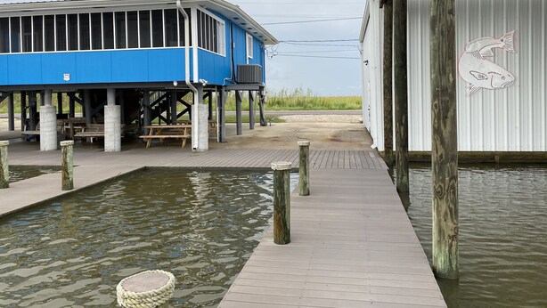 A waterfront building with a dock extending into the water, featuring a covered seating area and a fish mural. - Prime spot located on the water, Luxury living Bayou front living at its finest. (Chauvin)