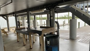 A covered outdoor area with picnic tables, a black barrel, and a staircase leading to a dock. - Prime spot located on the water, Luxury living Bayou front living at its finest. (Chauvin)