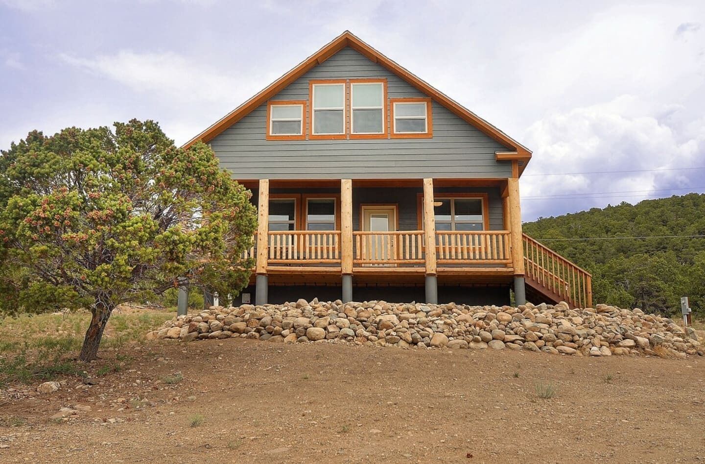 A two-story log cabin with a wooden deck and a stone foundation.