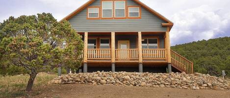 A two-story log cabin with a wooden deck and a stone foundation.