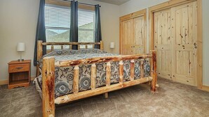 Une chambre à coucher avec un lit en bois, une table de chevet, une fenêtre avec des rideaux et des armoires en bois.
