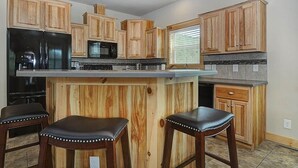 Une cuisine avec des meubles de rangement en bois, un réfrigérateur noir, un four à micro-ondes et un évier. On y trouve deux tabourets avec des clous en métal.