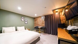 A hotel room with a large bed, a small table with two chairs, a brick wall, a TV, and a desk with a telephone. - Daeyeon Welkin Hotel (Busan)