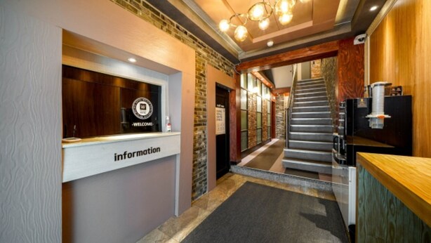 A reception area with a 'Welcome' sign, a reception desk labeled 'Information', a staircase leading to upper floors, and a coffee machine on the right. - Daeyeon Welkin Hotel (Busan)