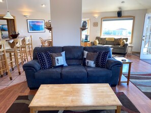A living room with a dark blue sofa, wooden coffee table, and a dining area with wooden chairs and a table.