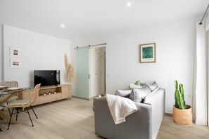 En moderne stue med sofa, TV, spiseplads og en kaktus.