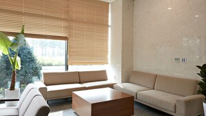 Un saló modern amb un sofà beix, una taula de centre de fusta i un gran finestral amb persianes.
