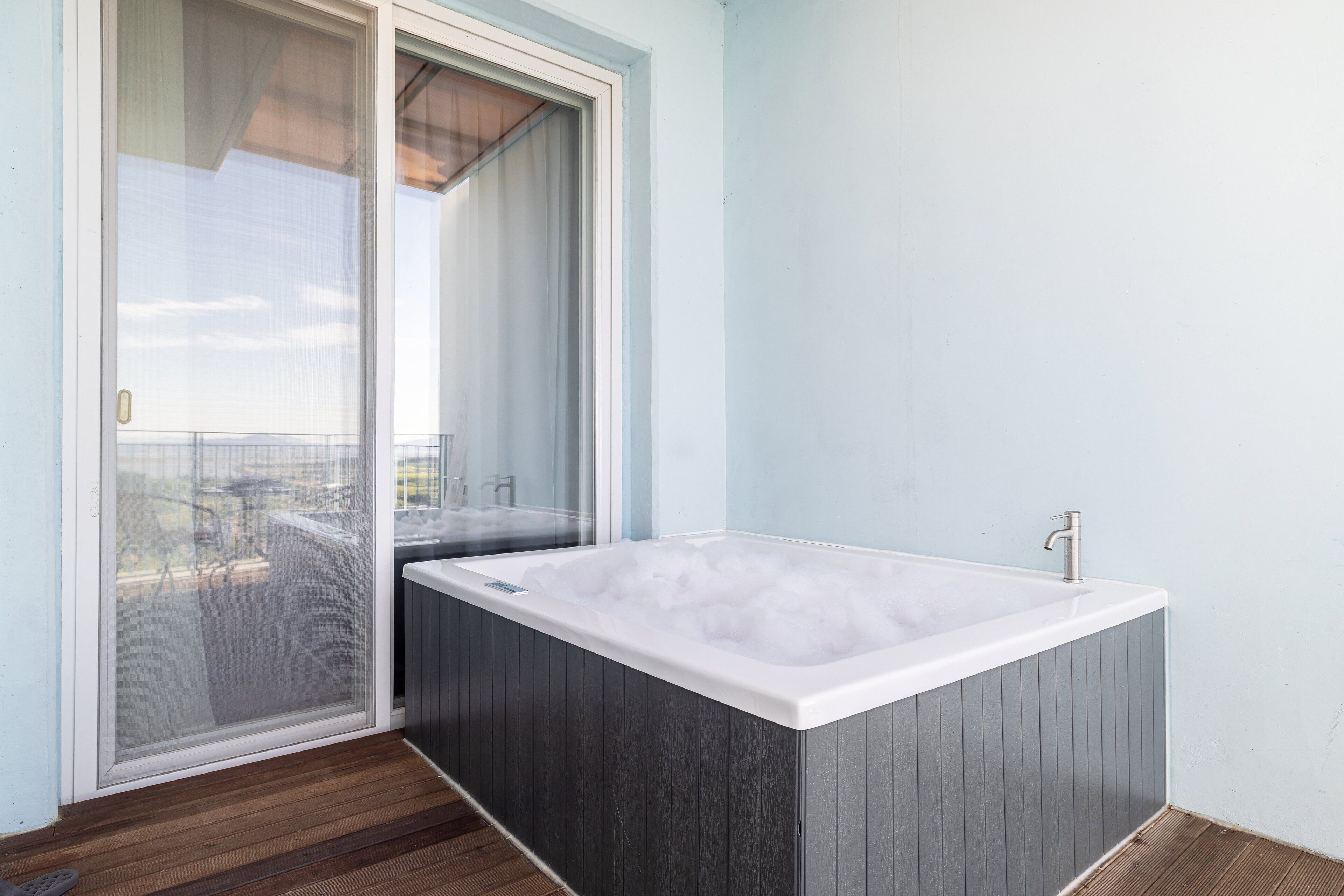 A modern bathroom with a large bathtub, a glass door leading to an outdoor area, and a wooden floor.