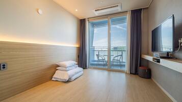 A modern hotel room with a large bed, a flat-screen TV, a small table, and a balcony with outdoor furniture.