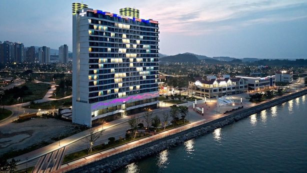 Un hotel alt amb nombroses plantes, vistes al mar i façana ben il·luminada.