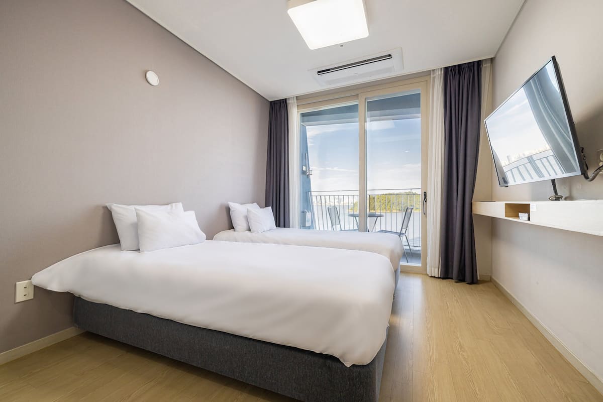 A hotel room with a large bed, a TV, a balcony with a view, and a window with curtains.