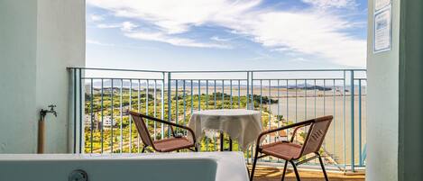 A balcony with a view of a beach and mountains, a small table, and two wicker chairs.