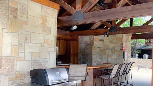 An outdoor kitchen area with a grill, stone walls, and a wooden ceiling. - Golf View Condo - Next to Dollywood (Pigeon Forge)