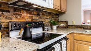 A kitchen with a stone backsplash, a stove, a microwave, and wooden cabinets. - Golf View Condo - Next to Dollywood (Pigeon Forge)