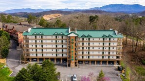 A multi-story hotel with a green roof, surrounded by a mountainous landscape. - Golf View Condo - Next to Dollywood (Pigeon Forge)