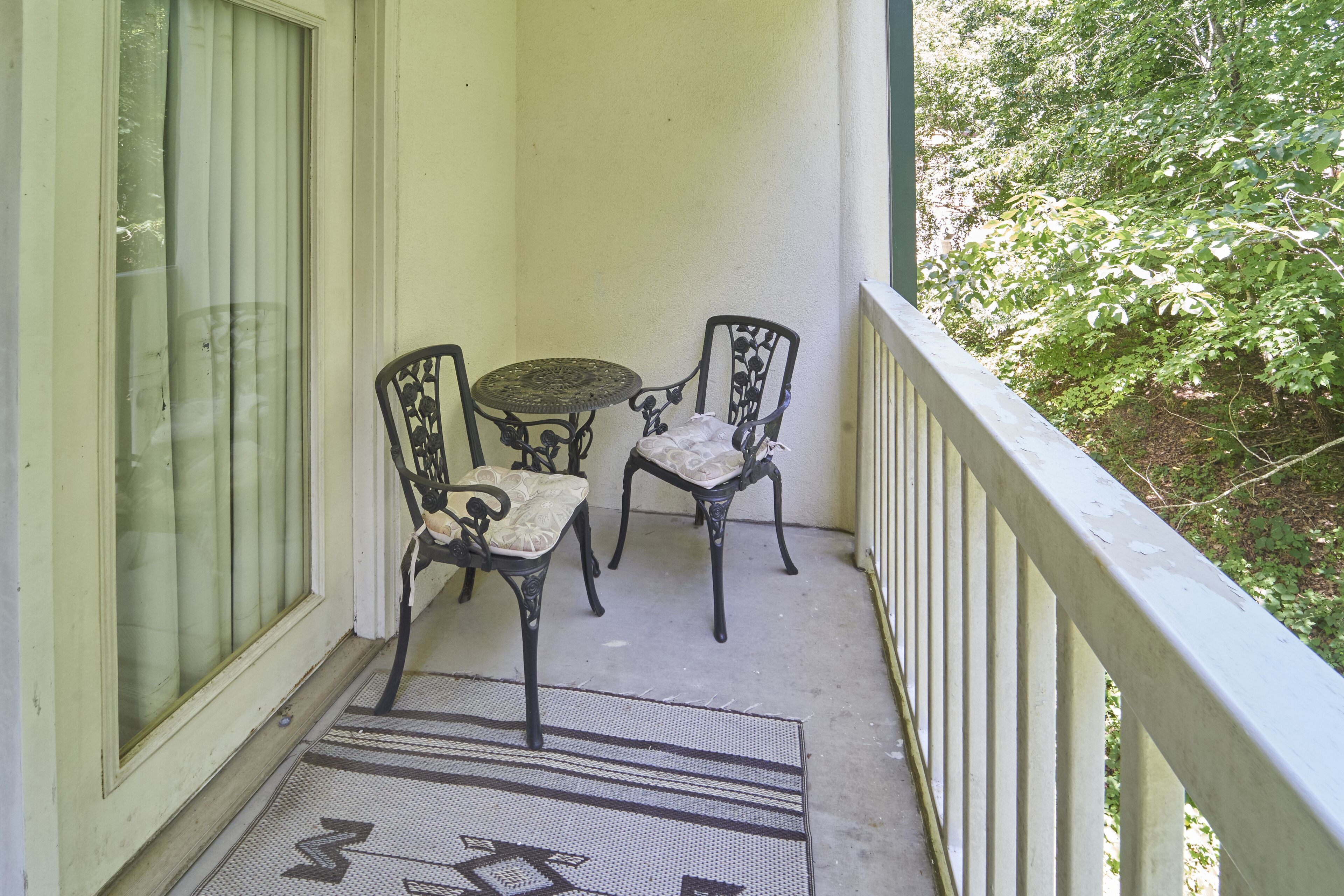 Un balcone con un tavolino, due sedie, un tappeto decorato e vista su zone verdi.
