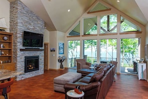 A spacious living room with a stone fireplace, leather sofa, and large windows offering a view of the outdoors.