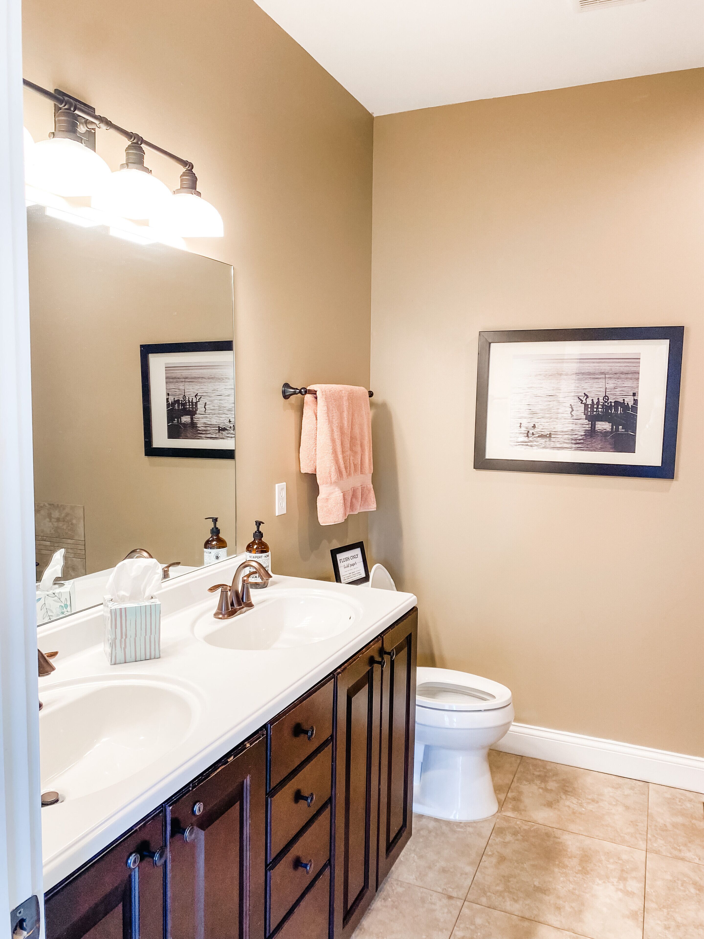 Une salle de bain avec un lavabo blanc, un miroir, des toilettes et deux tableaux encadrés accrochés au mur.