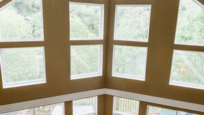 A room with multiple large windows offering views of a wooded area. - Spring Lily Retreat - Spacious, Lakefront, Hot Tub, Private Dock, Peaceful Cove! (Speedwell)