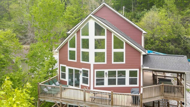 A two-story house with a balcony and a deck, surrounded by lush greenery. - Spring Lily Retreat - Spacious, Lakefront, Hot Tub, Private Dock, Peaceful Cove! (Speedwell)