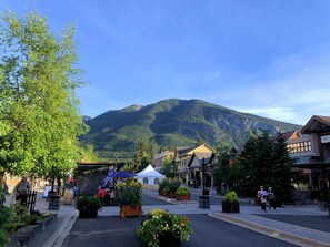 A town square with a mountain backdrop, outdoor seating, and a variety of shops and cafes. - Mountain View Escape - Top Floor (Canmore)