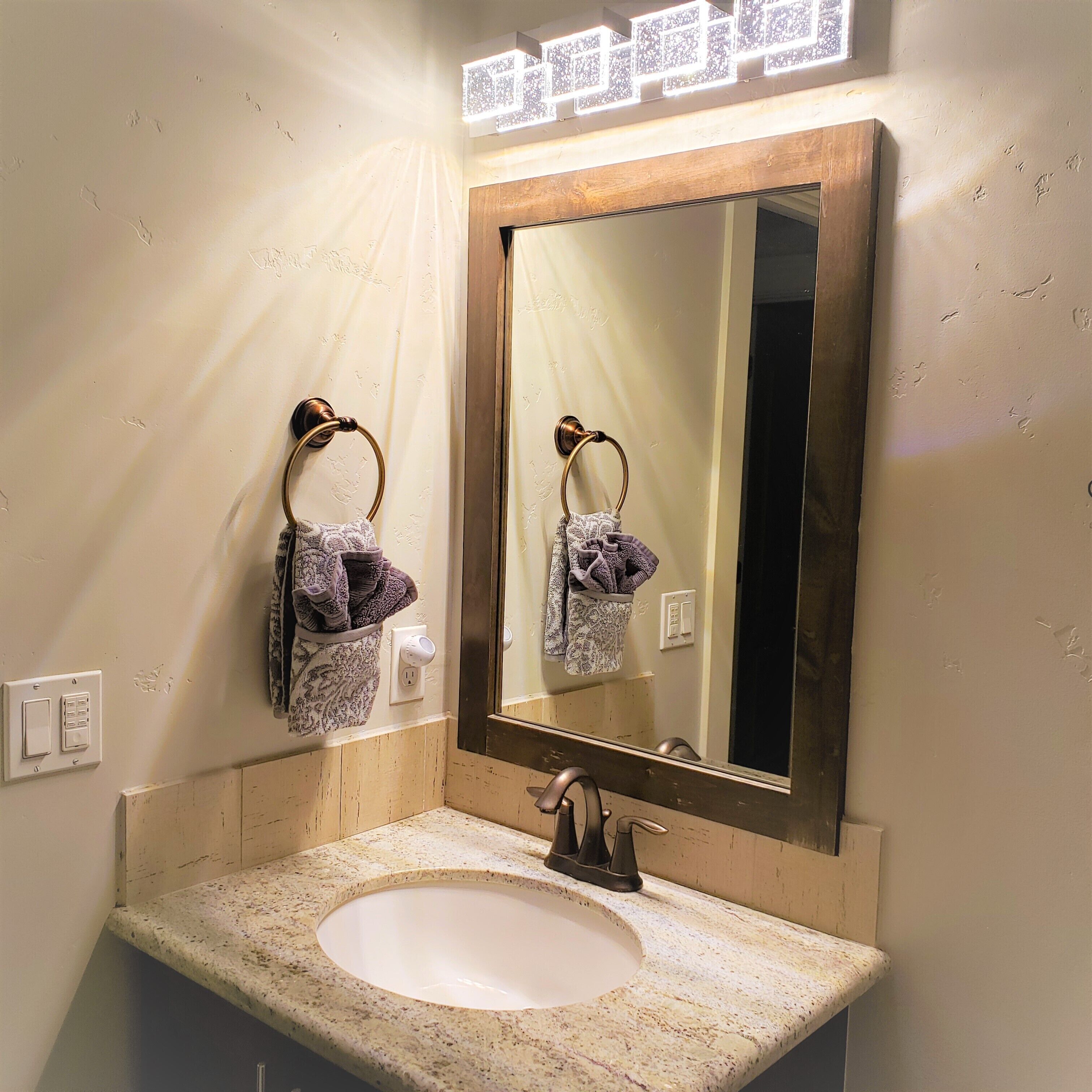 A bathroom with a large mirror, two towel rings, a sink, and a wall-mounted light fixture.