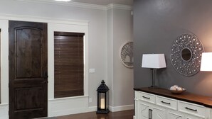 Une pièce avec une porte en bois, un plancher brun foncé, une armoire blanche avec des tiroirs, une lampe fixée au mur et une assiette décorative.